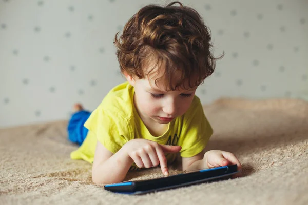 Kleine schattige jongen in een groen T-shirt spelen op een tablet en kijken cartoons. Peuter met tablet. — Stockfoto