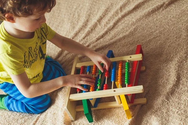 Hand eines kleinen Jungen, der mit Abakus spielt. Clouse up Bild von lockigen niedlichen Kleinkind spielen mit Holzspielzeug. Bildung für Kinder — Stockfoto