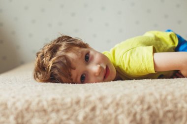 Yatakta yatarken ve seyir güzel bir çocuk. Kıvırcık şirin bebek