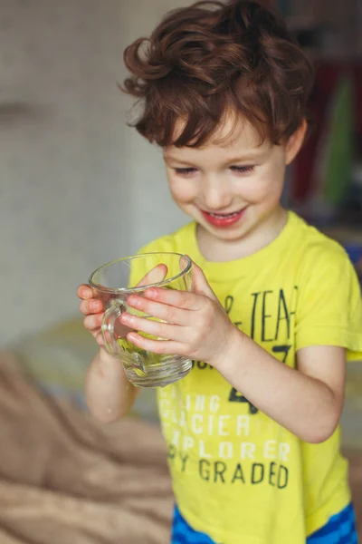 Маленький белый мальчик пьет воду в стакане дома. Милый кудрявый малыш пьет воду. Концепция здоровья — стоковое фото