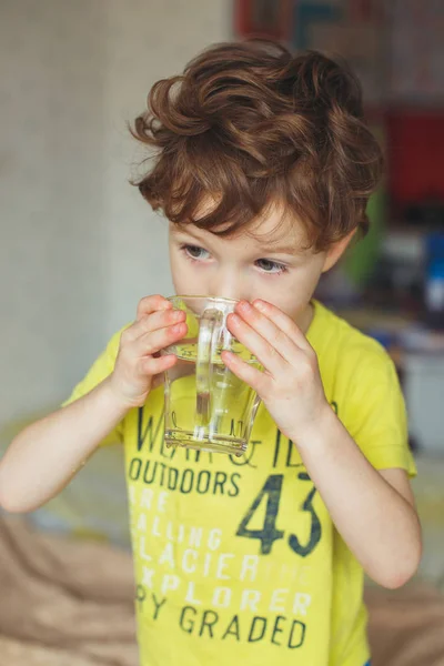 Мальчик, мальчик начинает свое утро со стакана пресной воды. Маленький кудрявый мальчик пьет воду. Концепция воды — стоковое фото