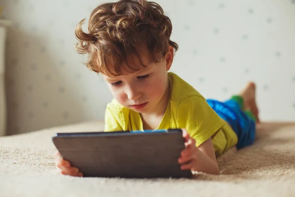 Schattige kleine jongen met behulp van een pad. Kind spelen met digitale tablet liggend op een bed. Vrije tijd. Tehnology en internet concept — Stockfoto