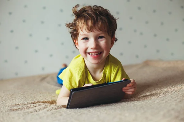 Маленький мальчик улыбается и смотрит на планшет, используя современные технологии — стоковое фото