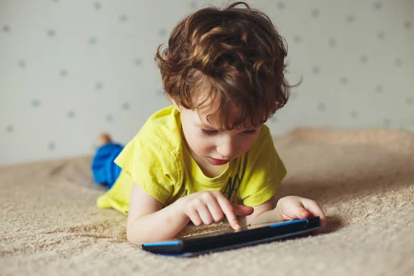 Kleiner Junge liegt auf dem Bett und schaut auf Tablet mit moderner Technik — Stockfoto