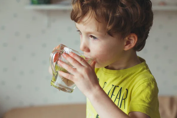 Маленький белый мальчик пьет воду в стакане дома. Милый кудрявый малыш пьет воду. Здоровье и вода — стоковое фото