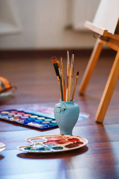 Paint Brushes on a table. Vertical photo. Easel, Canvas, paint, brushes, palette staying on the floor — Stock Photo, Image