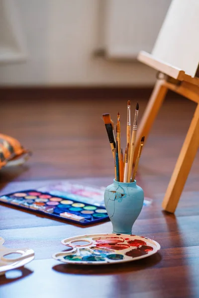 Paint Brushes on a table. Vertical photo. Easel, Canvas, paint, brushes, palette staying on the floor — Stock Photo, Image