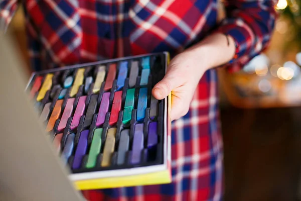 Set of multicolored pastel crayons in open artist box in woman hands. Artist painting on easel — Stock Photo, Image