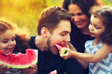 Mutlu bir aile yeşil bahçe piknik. Gülümseyen ve karpuz yeme insanlar gülüyor. Sağlık gıda kavramı. İkiz kardeşler