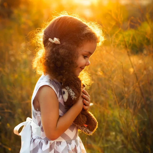 Menina sorridente adorável com brinquedo de coruja no parque. Noite ensolarada. Foto quadrada — Fotografia de Stock