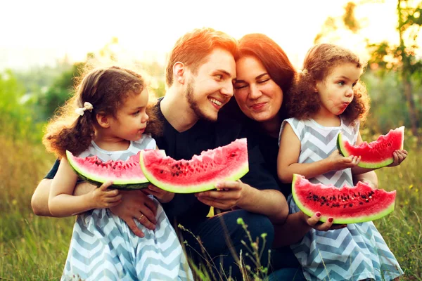 Familia feliz haciendo un picnic en el jardín verde. Sonriendo y riendo a la gente comiendo sandía. Concepto de comida saludable. Hermanas gemelas — Foto de Stock