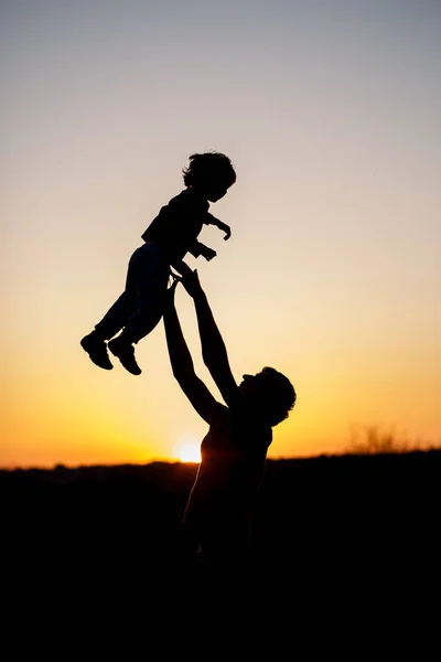 Silueta de un hombre y su hijo jugando juntos al aire libre al atardecer. Foto vertical. Concepto familiar — Foto de Stock