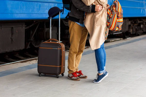 Pernas Amando Casal abraço feliz na estação de trem de um país após a chegada com um fundo de luz solar quente. Saco de carrinho de mão. Conceito de viagem — Fotografia de Stock