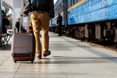 Seyahat kavramı. Erkek spor ayakkabı ayakkabı giymek ve sarı pantolon kahverengi bavullarla mı seyahat ve tren istasyonunda sırt çantası. Güneşli gün.