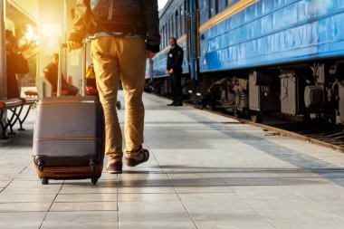 Seyahat kavramı. Erkek spor ayakkabı ayakkabı giymek ve sarı pantolon kahverengi bavullarla mı seyahat ve tren istasyonunda sırt çantası. Güneşli gün.