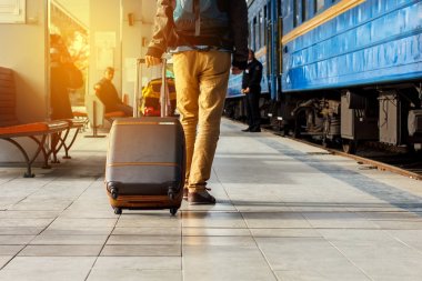 Seyahat kavramı. Erkek spor ayakkabı ayakkabı giymek ve sarı pantolon kahverengi bavullarla mı seyahat ve tren istasyonunda sırt çantası. Güneşli gün.