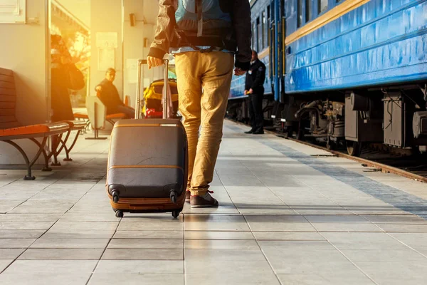 Conceito de viagem. Os homens usam tênis e calças amarelas viajam com bagagem marrom e mochila na estação de trem. Dia ensolarado . — Fotografia de Stock