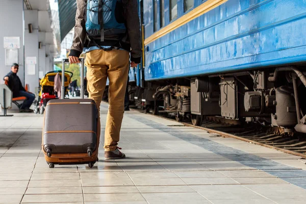 Conceito de viagem. Os homens usam tênis e calças amarelas viajam com bagagem marrom e mochila na estação de trem. Dia ensolarado . — Fotografia de Stock