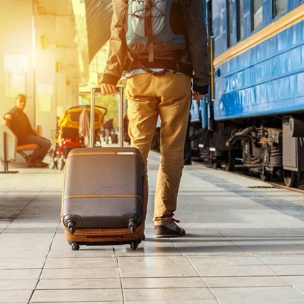 Conceito de viagem. Os homens usam tênis e calças amarelas viajam com bagagem marrom e mochila na estação de trem. Dia ensolarado . — Fotografia de Stock