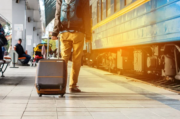 Concepto de viaje. Los hombres usan zapatillas de deporte y los pantalones amarillos viajan con equipaje marrón y mochila en la estación de tren. Día soleado . — Foto de Stock