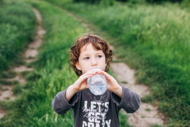 Çocuk doğada saf su içme. Sevimli kıvırcık yürümeye başlayan çocuk