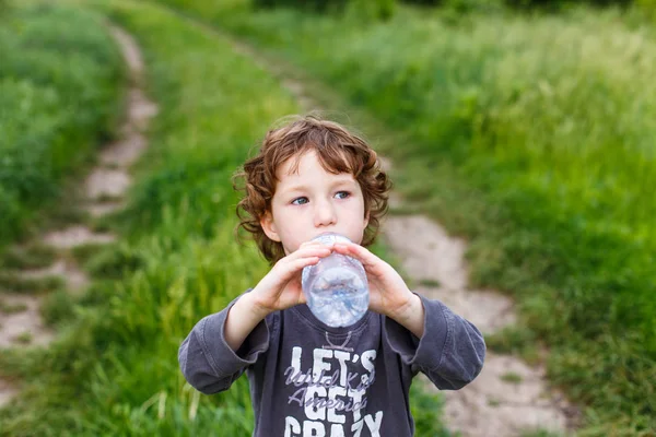 Ребенок пьет чистую воду в природе. Милый кудрявый малыш — стоковое фото