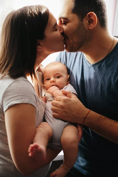 Tânăra mamă și tatăl se sărută unul pe altul cu copilul pe mâini. Închide portretul. Conceptul de familie fericit — Fotografie, imagine de stoc