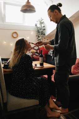 Romantic couple having dinner at home. Man pouring wine. Beautiful cozy interior