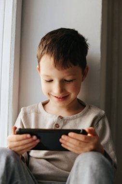 Küçük gülümseyen çocuk oyun oynuyor ya da dijital akıllı telefon bilgisayarında internette sörf yapıyor.