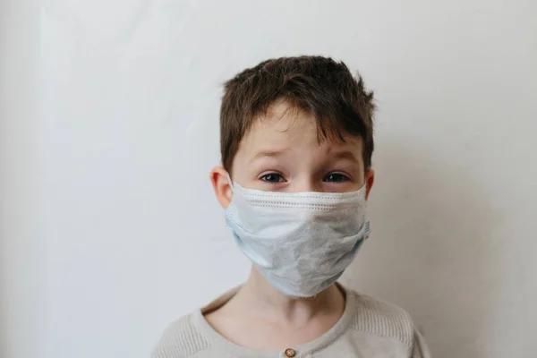 Niño llorón con máscara médica en la cara. Brote de virus corona Covid 2019. Niño triste aislado en blanco. Niño en casa —  Fotos de Stock