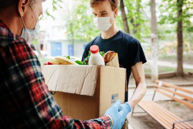 Baget ekmeği ve taze sebzeleri poşete koy. Kurye, yaşlı beyaz adama yemek getiriyor ve açık havada dağıtıyor. Teslimatçı, erkek emekliye bakkal getiriyor..