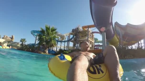 Homem branco em anel de borracha flutuando no rio no parque aquático. Slides no fundo — Vídeo de Stock