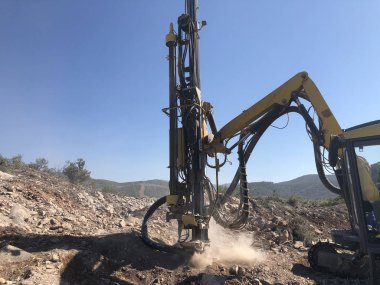 Sarı makineler, patlama deliği delme operasyonları sırasında kayalık deniz uçurumunda delikler açıyor.