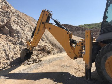 Yellow loader backhoe digs a trench during road construction works. Earthmoving, excavations, digging on the rocky soils