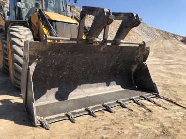 Bucket of yellow loader backhoe digging a trench during road construction works. Earthmoving, excavations, digging