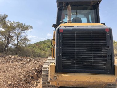 Sürüngen buldozer arkadan geliyor. Yol inşaatında yer değiştiren ağır makineler