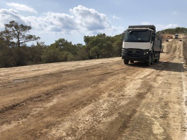 Kamyon kazılmış toprak taşıyor. Yol inşaatında farklı makineler kullanılıyor