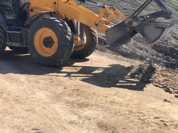A retroescavadeira do carregador amarelo está planejando uma superfície de estrada durante as obras de construção de estradas. terraplanagem, escavações, escavação — Fotografia de Stock