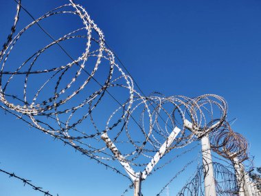 Çitin üzerindeki dikenli tel açık mavi gökyüzünün karşısında
