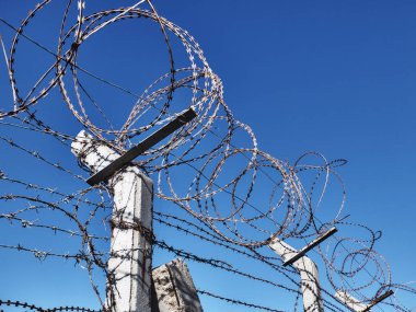 Çitin üzerindeki dikenli tel açık mavi gökyüzünün karşısında