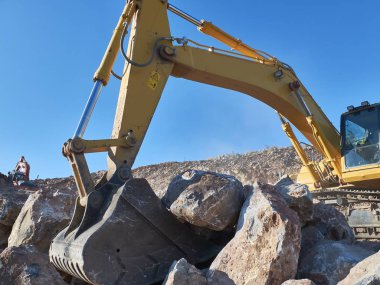 Excavator is moving a rock boulders during road construction on the rocky soils clipart