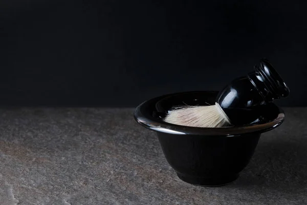 Escova de barbear e tigela na superfície de pedra em fundo preto — Fotografia de Stock