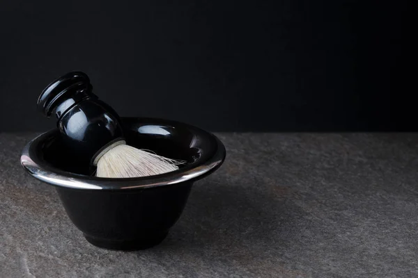 Escova de barbear e tigela na superfície de pedra em fundo preto — Fotografia de Stock