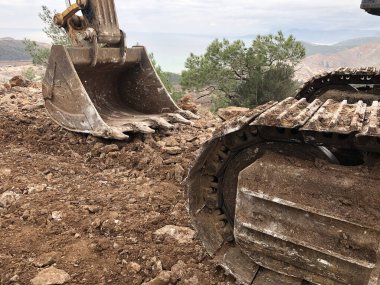 Kazıcı kepçesi kayalık topraklardaki yol inşaatı sırasında toprağı düzleştirir. Toprak taşıma, kazma ve kazı işlemlerinde ağır makineler.