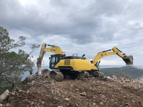 Excavator and hydrohammer during road construction on the rocky soils. Heavy machinery at earthmoving, digging, excavation operations.