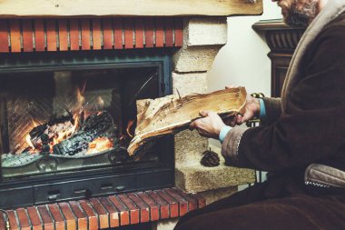 man with beard wearing bathrobe puts log in burning fireplace clipart