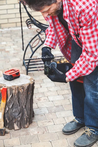 Man in plaid shirt inserts in electric saw handsaw — Stock Photo, Image