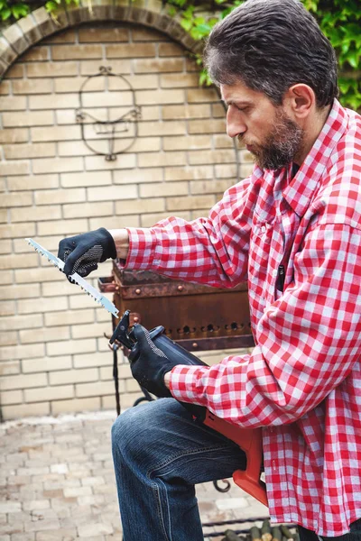 Homme en chemise à carreaux inserts en scie à main électrique — Photo