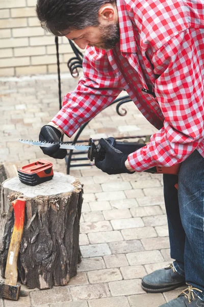 Man in plaid shirt inserts in electric saw handsaw — Stock Photo, Image