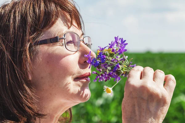 Happy elderly woman smelling bouquet of wildflowers — Stock Photo, Image